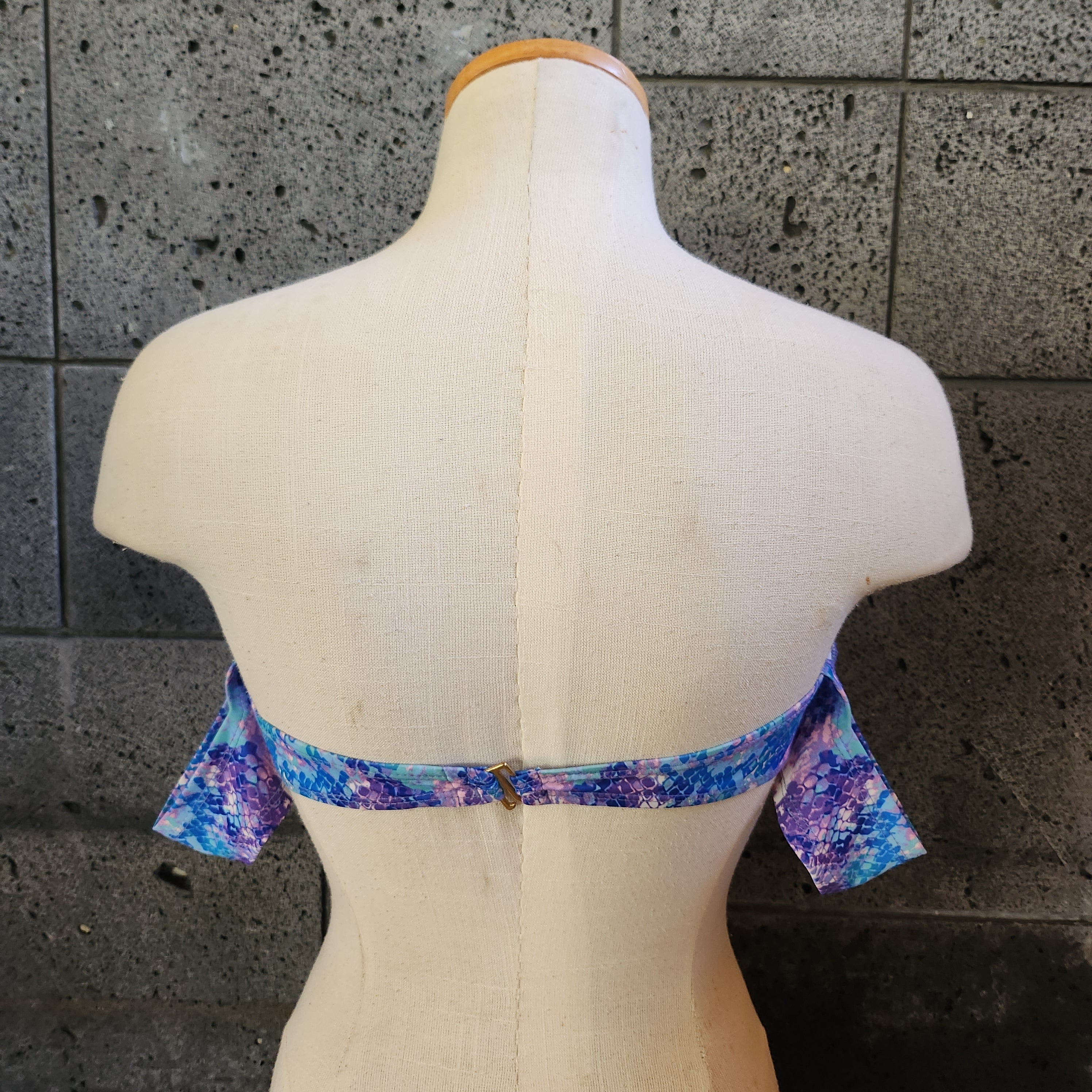 Colorful swimsuit on a mannequin against a dark tiled wall.