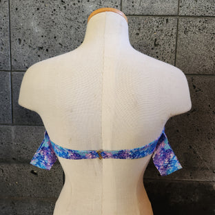 Colorful swimsuit on a mannequin against a dark tiled wall.