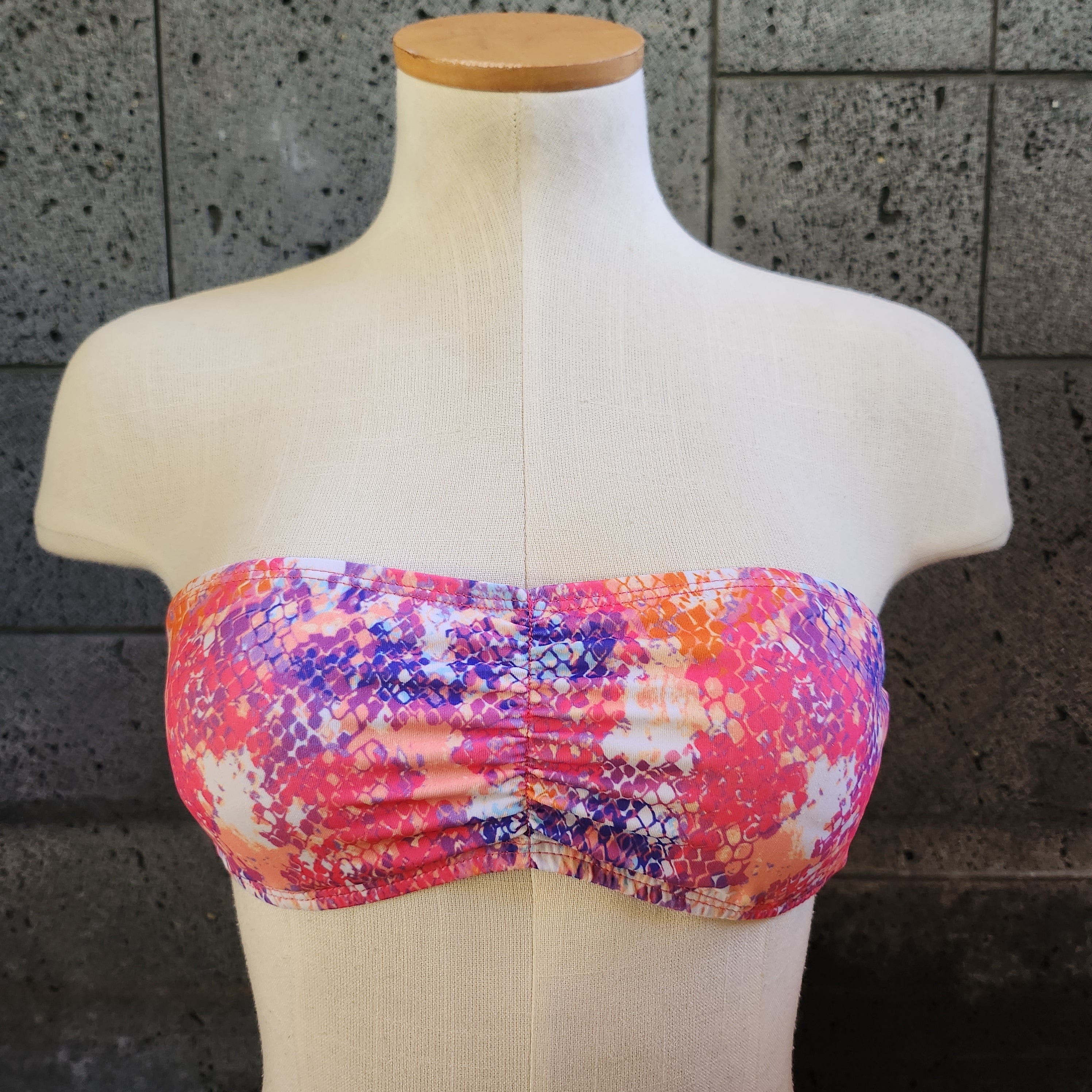 Colorful swimsuit on a mannequin against a dark tiled wall.