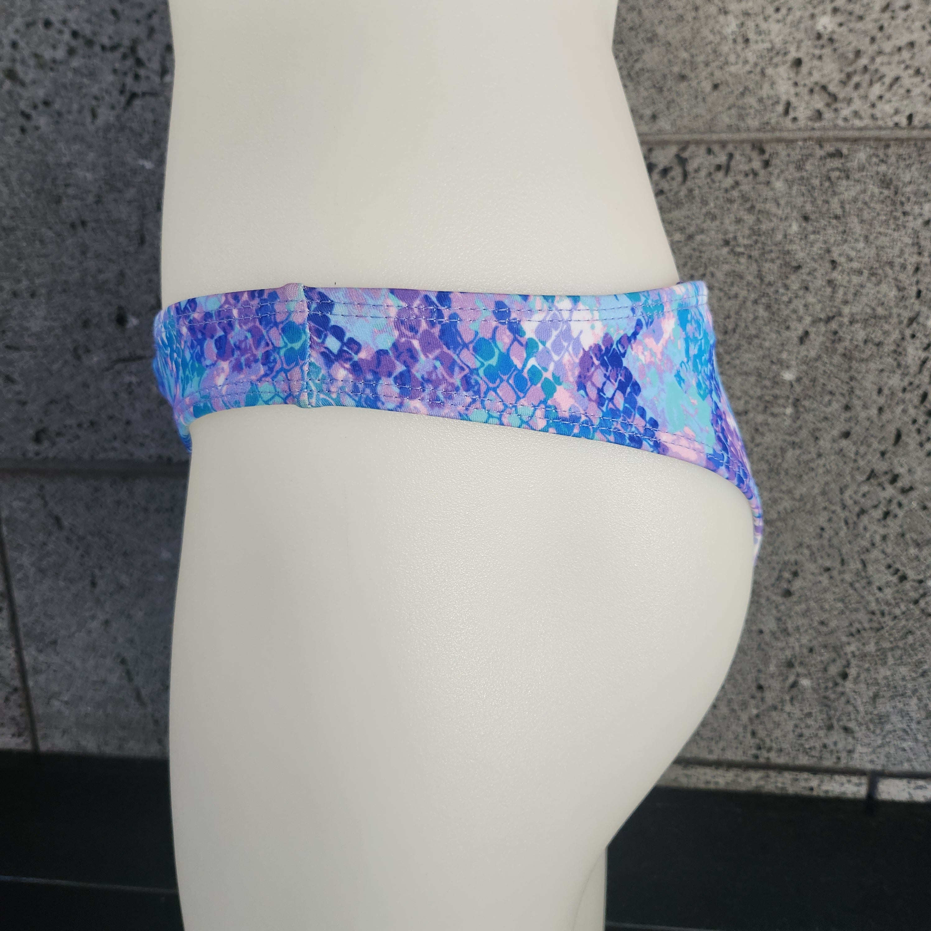 Colorful bikini bottom on a mannequin against a gray concrete wall.