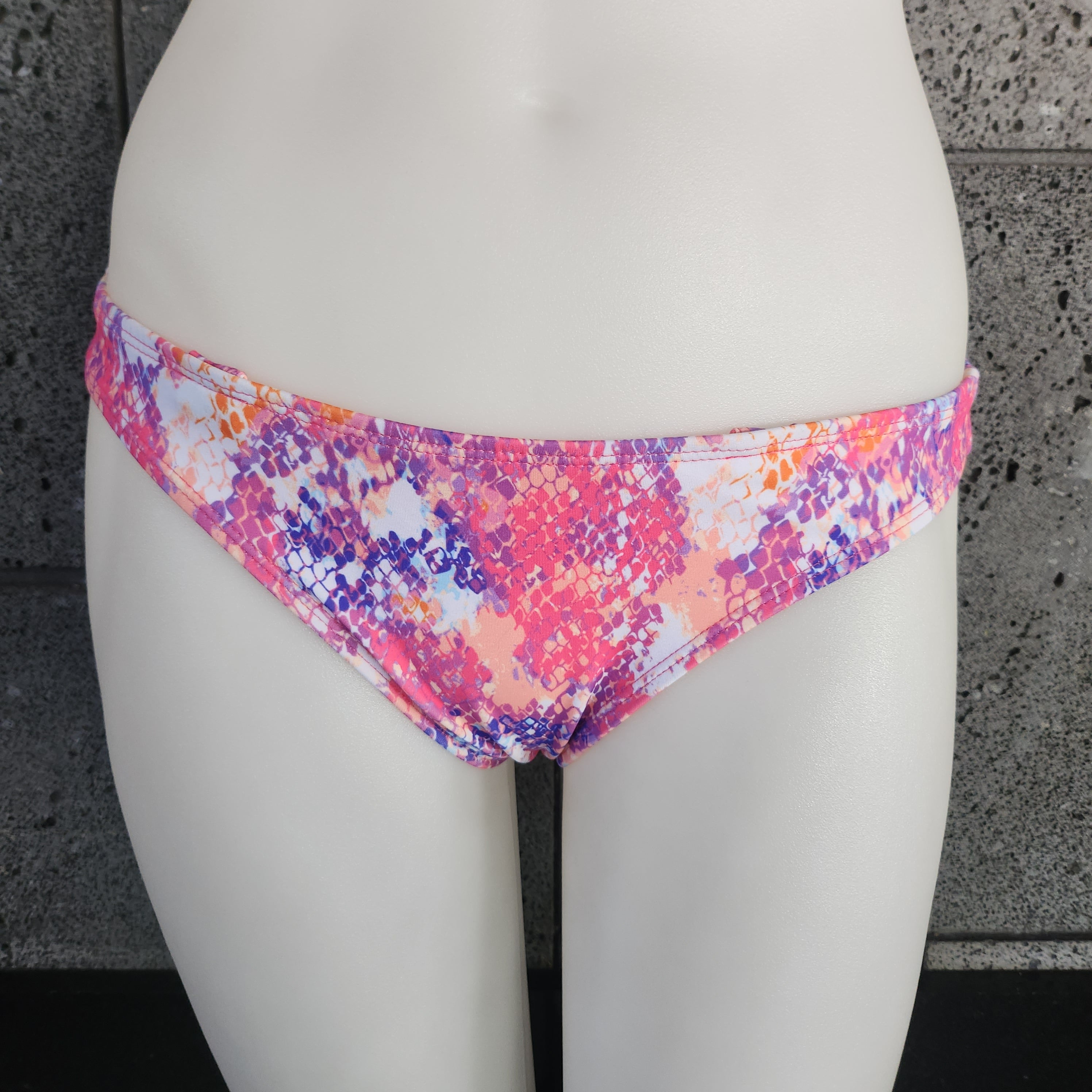 Colorful bikini bottom on a mannequin against a gray concrete wall.