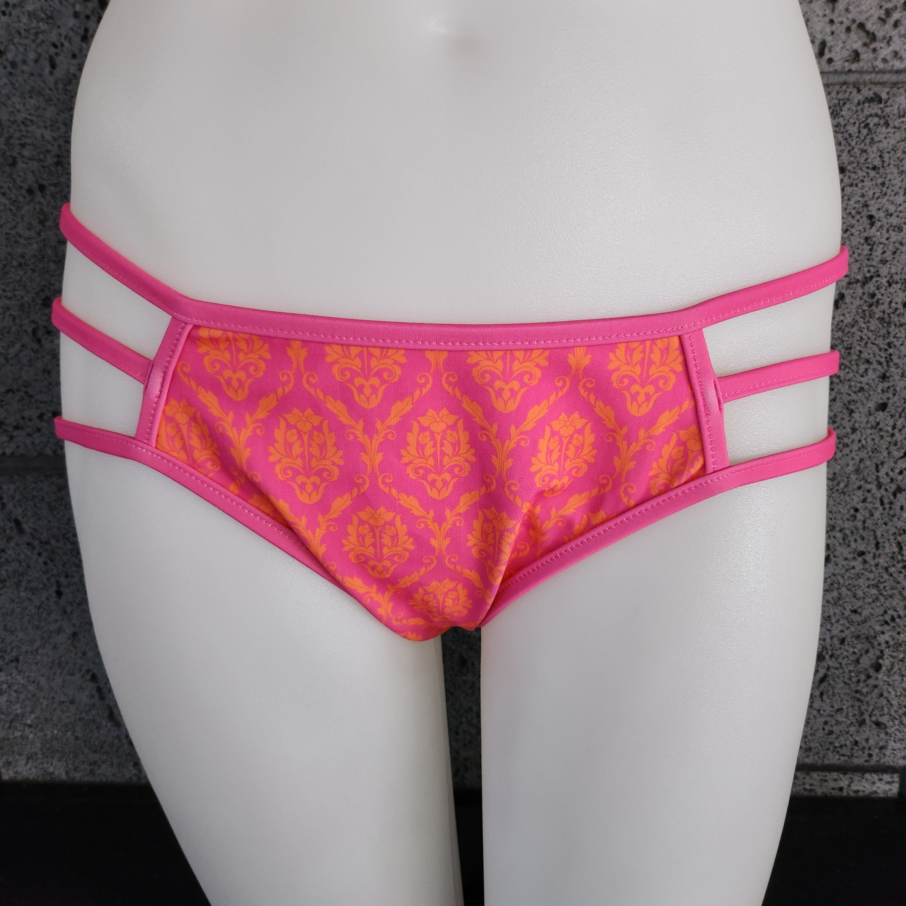 Pink and orange patterned bikini bottom on a mannequin against a dark background