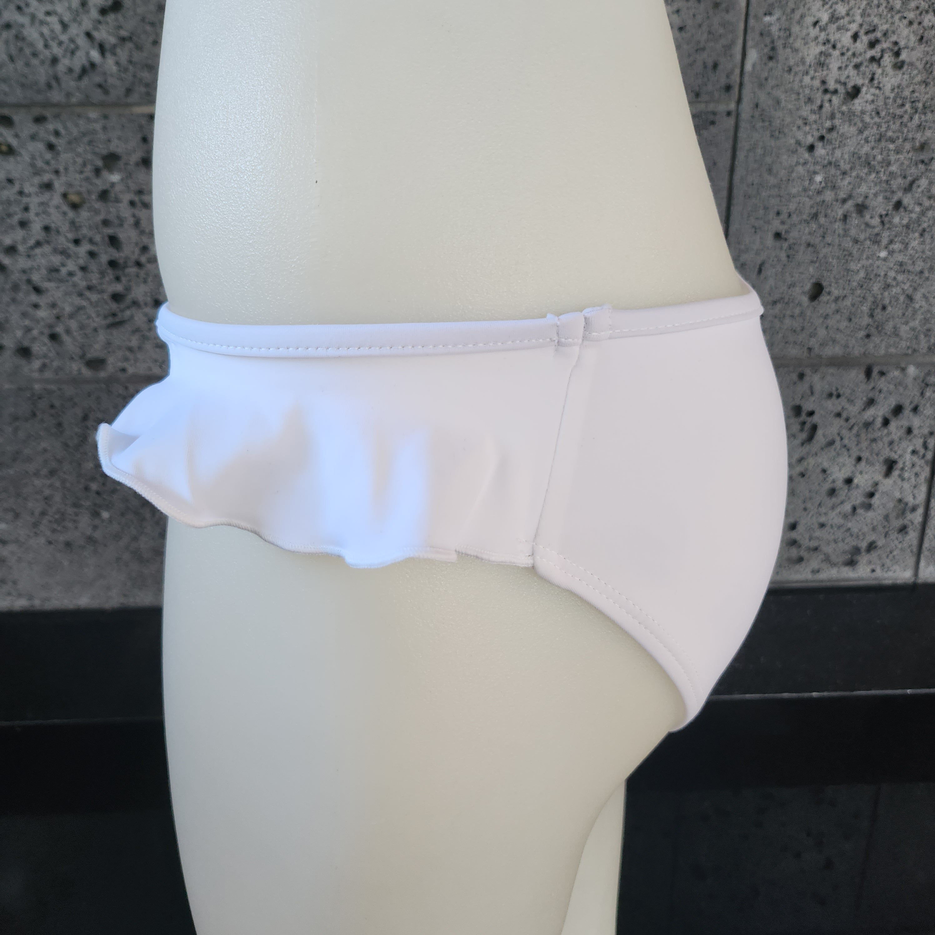 Navy blue bikini bottom on a mannequin against a gray tiled wall.