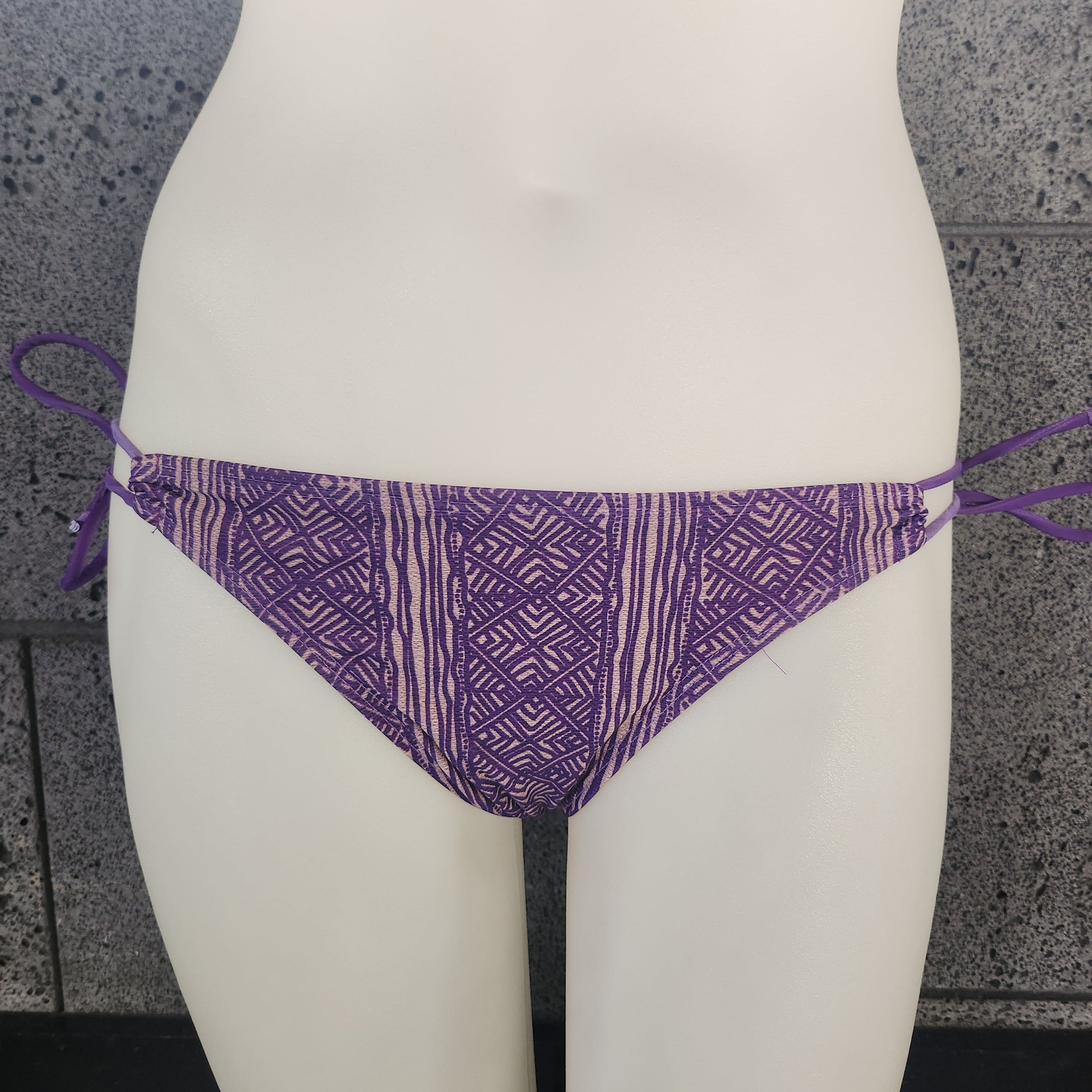 Purple patterned bikini top on a mannequin against a gray background