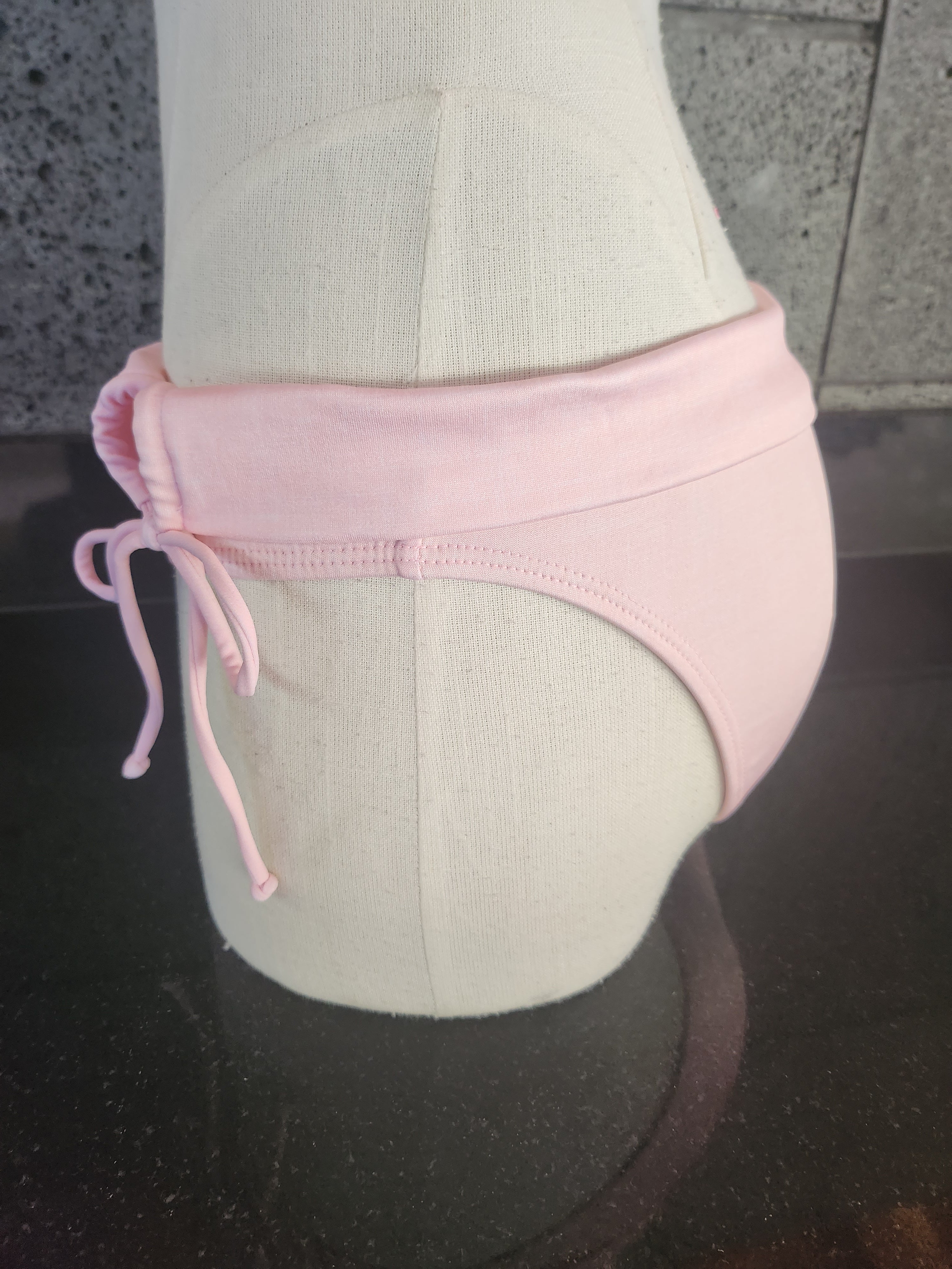 A swimwear garment with a folded over waistband and side gathered design, displayed on a mannequin.