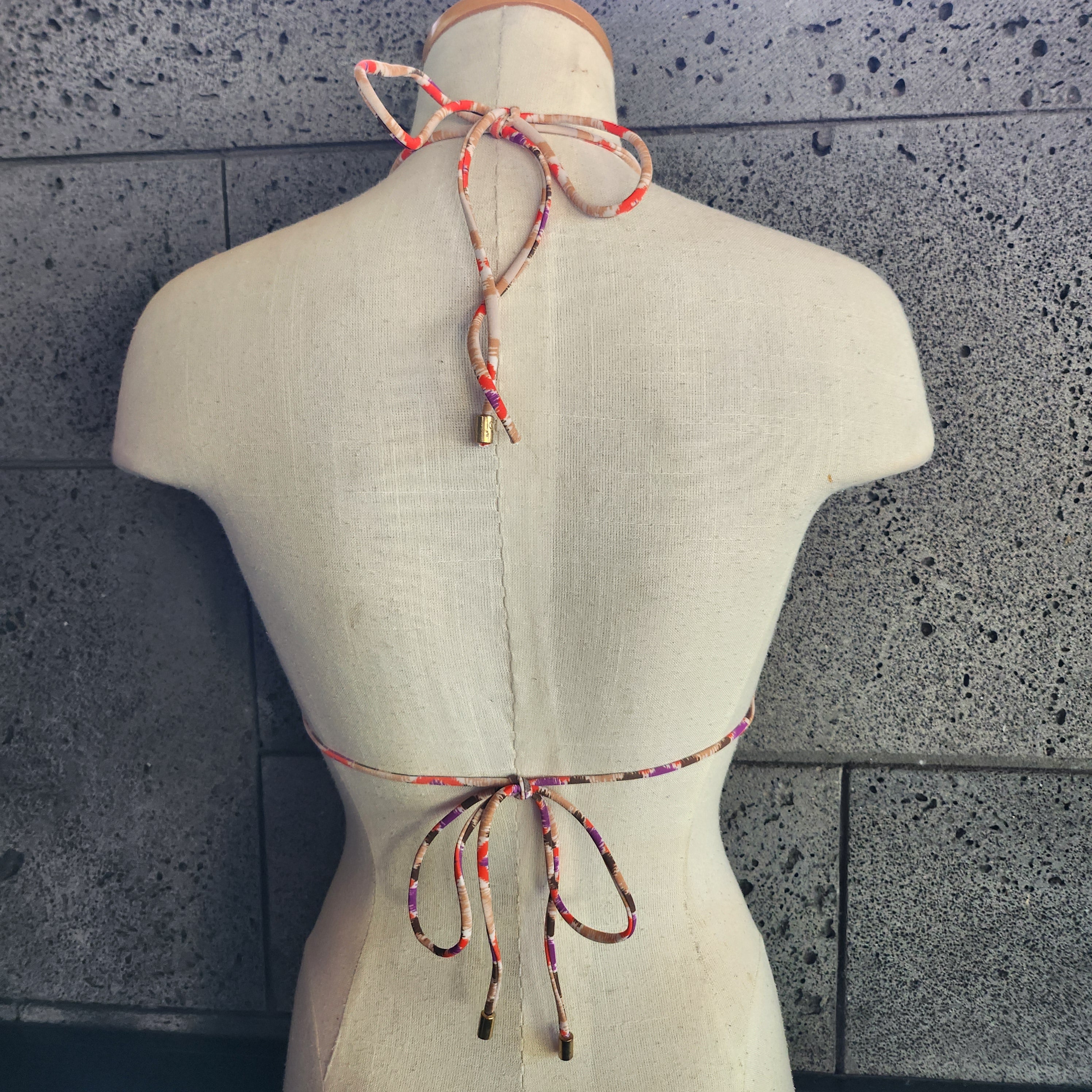 Colorful patterned bikini on a mannequin against a gray tiled floor background