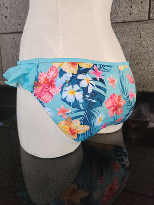 A bikini bottom with a Hawaiian flower print and a side ruffle detail, displayed on a mannequin.