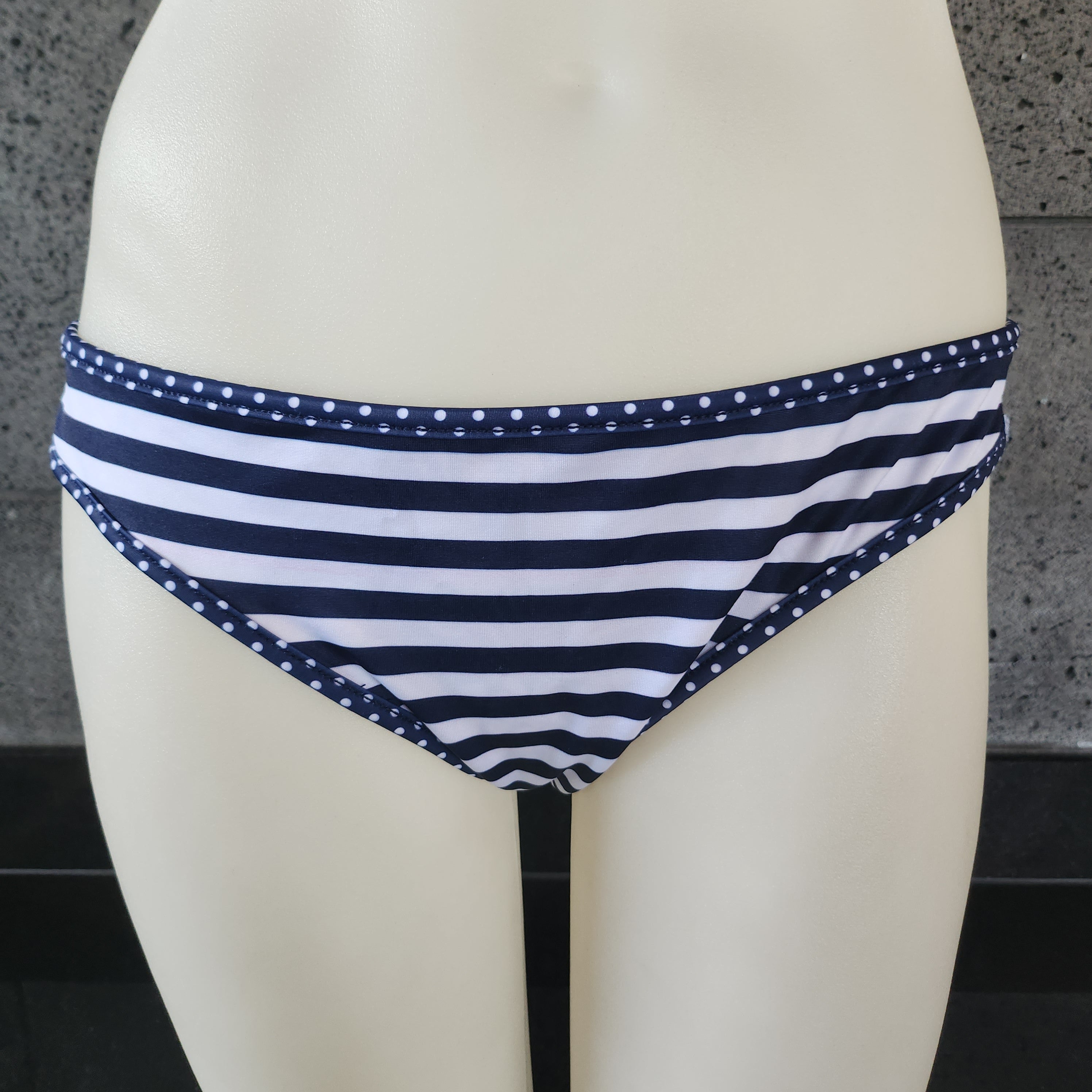 Red and white patterned bikini bottom on a mannequin against a tiled wall.